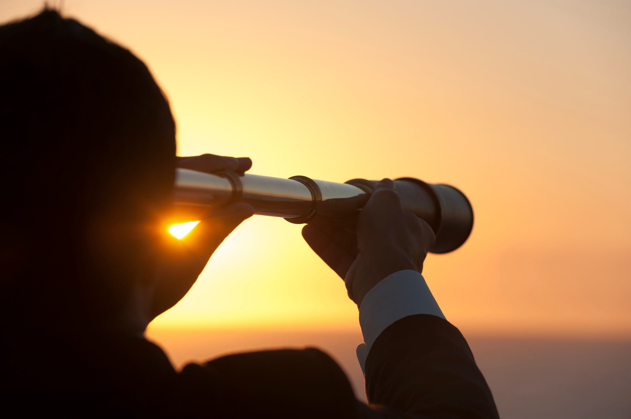 The silhouette of a man observing through binoculars against a stunning sunset backdrop